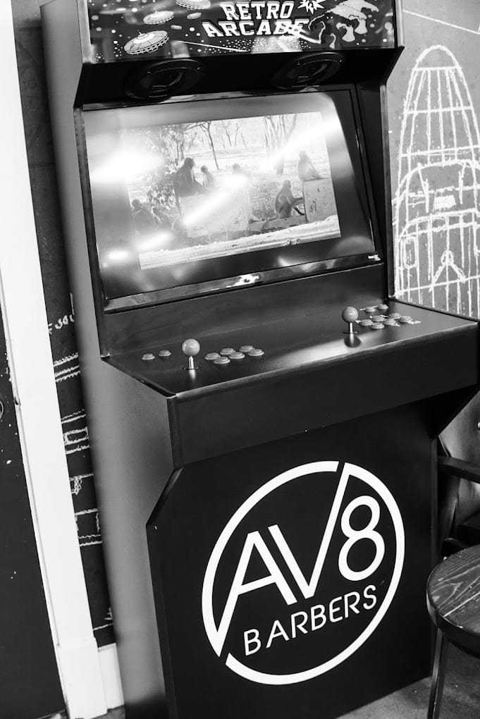 Arcade machine at AV8 Barbers with a displayed game screen, set in a vintage style shop.